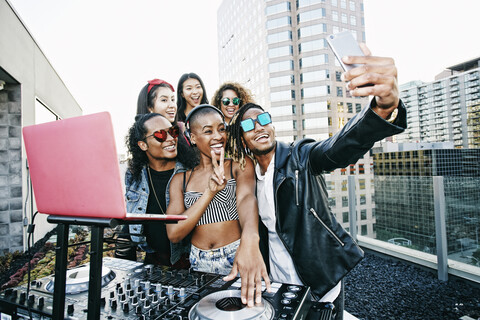 Friends posing for cell phone selfie with DJ on urban rooftop stock photo