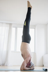 Older Caucasian man doing headstand on exercise mat - BLEF03528