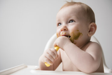 Unordentliches kaukasisches Baby isst vom Löffel im Hochstuhl - BLEF03545