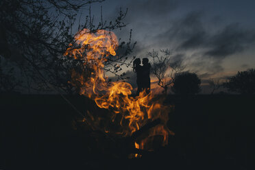 Silhouette eines kaukasischen Paares, das sich in der Nähe des Feuers küsst - BLEF03585