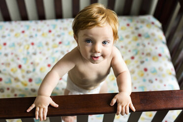 Portrait of curious Caucasian baby boy standing in crib - BLEF03604