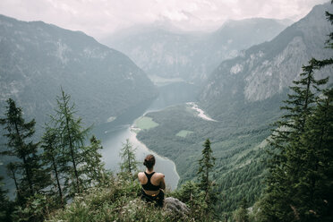 Kaukasische Frau sitzt auf einem Felsen mit Blick auf einen See in einem Tal - BLEF03620