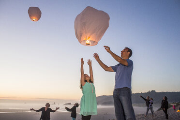 Caucasian father and daughter flying lantern balloon at beach - BLEF03641