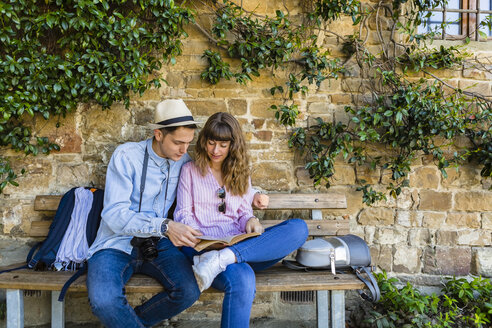 Junges Paar auf Städtereise, sitzt auf einer Bank und liest einen Reiseführer - MGIF00419