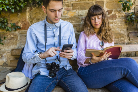Junges Paar auf Städtereise, sitzt auf einer Bank und liest einen Reiseführer, lizenzfreies Stockfoto