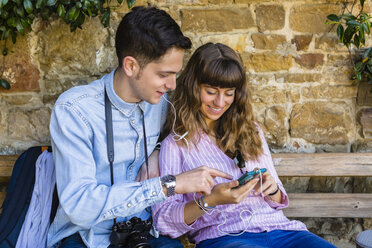 Junges Paar auf Städtereise, auf einer Bank sitzend, mit Smartphone - MGIF00423