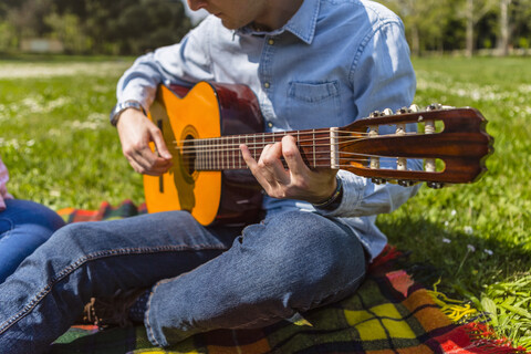 Junger Mann spielt Gitarre in einem Park, lizenzfreies Stockfoto