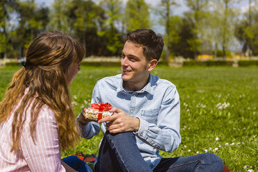 Young woman gifting her boyfriend with a present in a park - MGIF00468