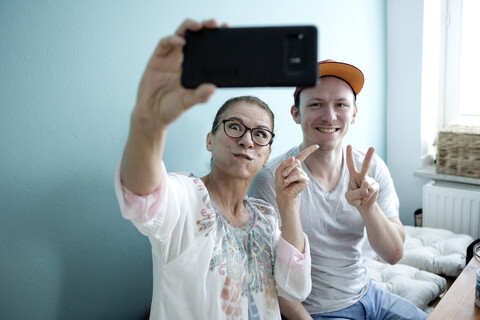 Mutter und Sohn sitzen am Küchentisch und machen Selfies mit ihrem Smartphone, lizenzfreies Stockfoto