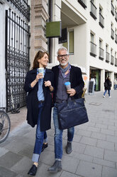 Smiling mature couple with reusable bamboo cups walking in the city - ECPF00736