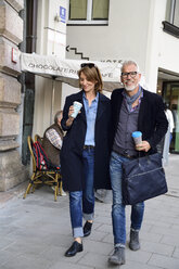 Smiling mature couple with reusable bamboo cups walking in the city - ECPF00737