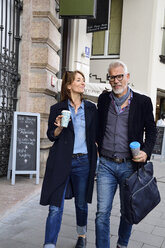 Smiling mature couple with reusable bamboo cups walking in the city - ECPF00738