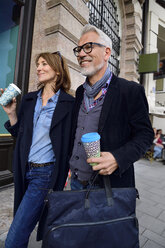 Smiling mature couple with reusable bamboo cups walking in the city - ECPF00739