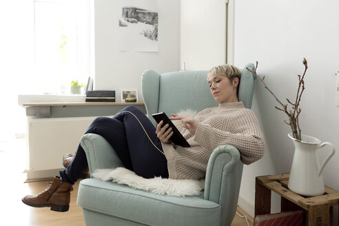 Relaxed woman sitting in armchair at home using tablet - FLLF00157