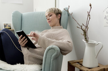 Relaxed woman sitting in armchair at home using tablet - FLLF00158