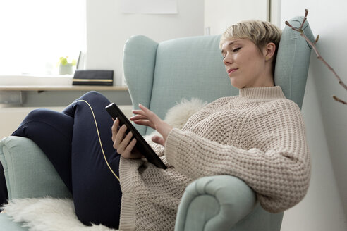 Entspannte Frau, die zu Hause im Sessel sitzt und ein Tablet benutzt - FLLF00159