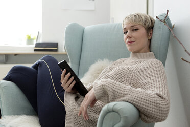 Portrait of woman sitting in armchair at home with tablet - FLLF00160