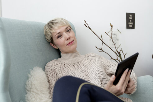 Porträt einer Frau, die zu Hause in einem Sessel sitzt und ein Tablet benutzt - FLLF00162