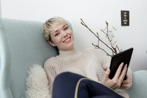Porträt einer Frau, die zu Hause in einem Sessel sitzt und ein Tablet benutzt - FLLF00163