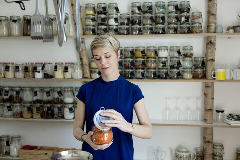 Woman opening jar in front of spice shelf in kitchen stock photo