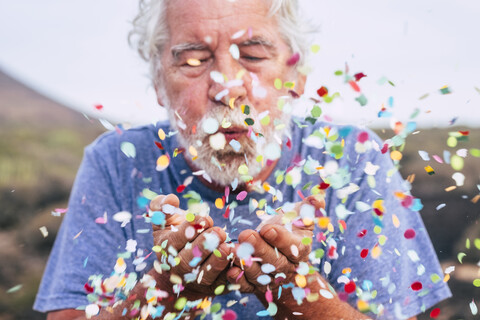 Älterer Mann bläst Konfetti im Freien, lizenzfreies Stockfoto