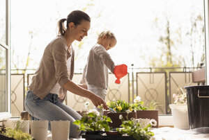 Mother and daughter planting flowers together on balcony - DIGF07051