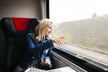 Lächelnde blonde Frau, die mit dem Zug reist und aus dem Fenster schaut - HMEF00374