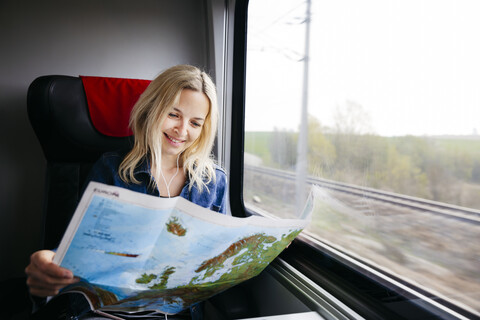 Portrait of happy blond woman travelling by train looking at map of Europe stock photo