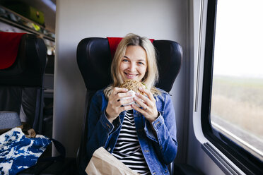 Porträt einer lächelnden blonden Frau, die mit dem Zug reist und einen Snack zu sich nimmt - HMEF00384