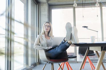 Entspannte Geschäftsfrau, die im Büro einen Laptop benutzt und die Füße hochlegt - UUF17462