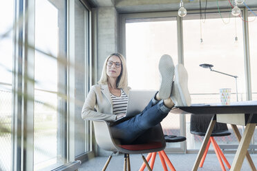 Relaxed businesswoman using laptop in office with feet up - UUF17462