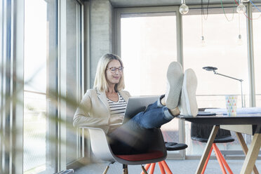 Relaxed businesswoman using laptop in office with feet up - UUF17463