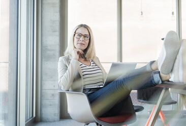 Relaxed businesswoman using laptop in office with feet up - UUF17464