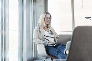 Relaxed businesswoman using laptop in office with feet up - UUF17465