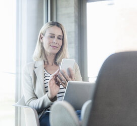 Relaxed businesswoman using cell phone in office with feet up - UUF17467