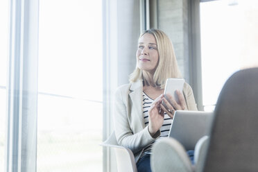 Relaxed businesswoman using cell phone in office with feet up - UUF17468