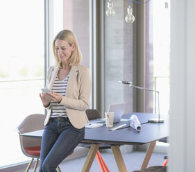 Lächelnde Geschäftsfrau, die im Büro ein Mobiltelefon benutzt - UUF17475