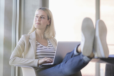 Relaxed businesswoman using laptop in office with feet up - UUF17478