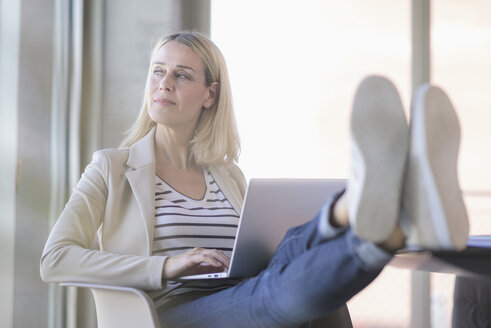Entspannte Geschäftsfrau, die im Büro einen Laptop benutzt und die Füße hochlegt - UUF17478