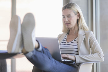 Relaxed businesswoman using laptop in office with feet up - UUF17479