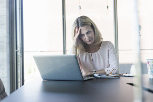 Stressed businesswoman using laptop in office - UUF17495