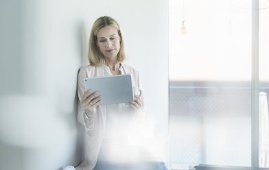 Businesswoman leaning against a wall using tablet - UUF17497