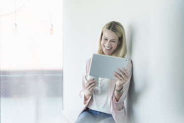 Glückliche Geschäftsfrau lehnt an einer Wand und benutzt ein Tablet - UUF17498