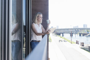 Lässige Geschäftsfrau, die auf einem Balkon steht und ein Tablet benutzt - UUF17501