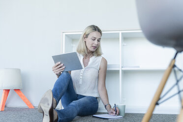 Lässige Geschäftsfrau, die im Büro auf dem Boden sitzt, ein Tablet benutzt und Notizen macht - UUF17502