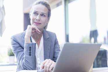 Businesswoman using laptop at an outdoor cafe - UUF17518