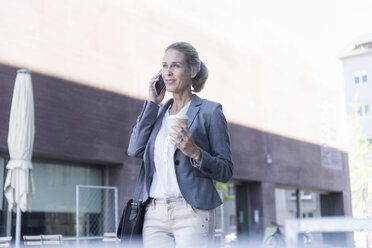 Geschäftsfrau mit Mobiltelefon und Kaffee zum Mitnehmen unterwegs in der Stadt - UUF17519