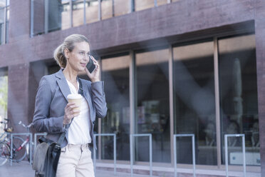 Businesswoman with cell phone and takeaway coffee on the go in the city - UUF17521