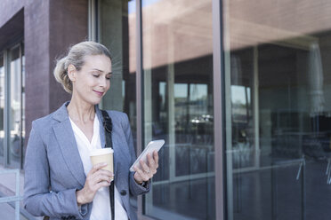 Geschäftsfrau mit Mobiltelefon und Kaffee zum Mitnehmen unterwegs in der Stadt - UUF17525