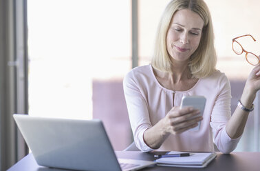 Geschäftsfrau benutzt Mobiltelefon im Büro - UUF17530